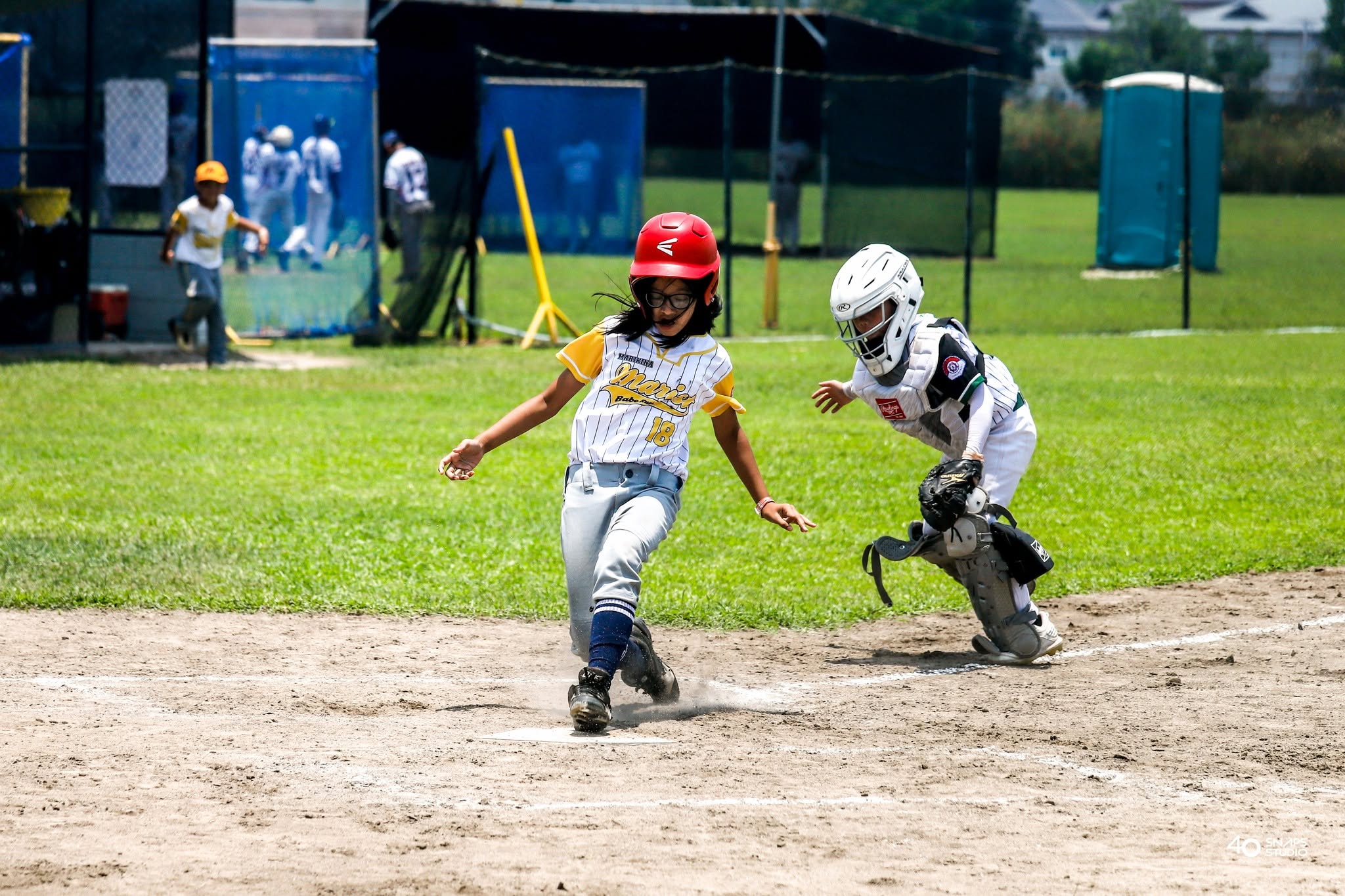 Young baseball player running home as a catcher reaches for the ball